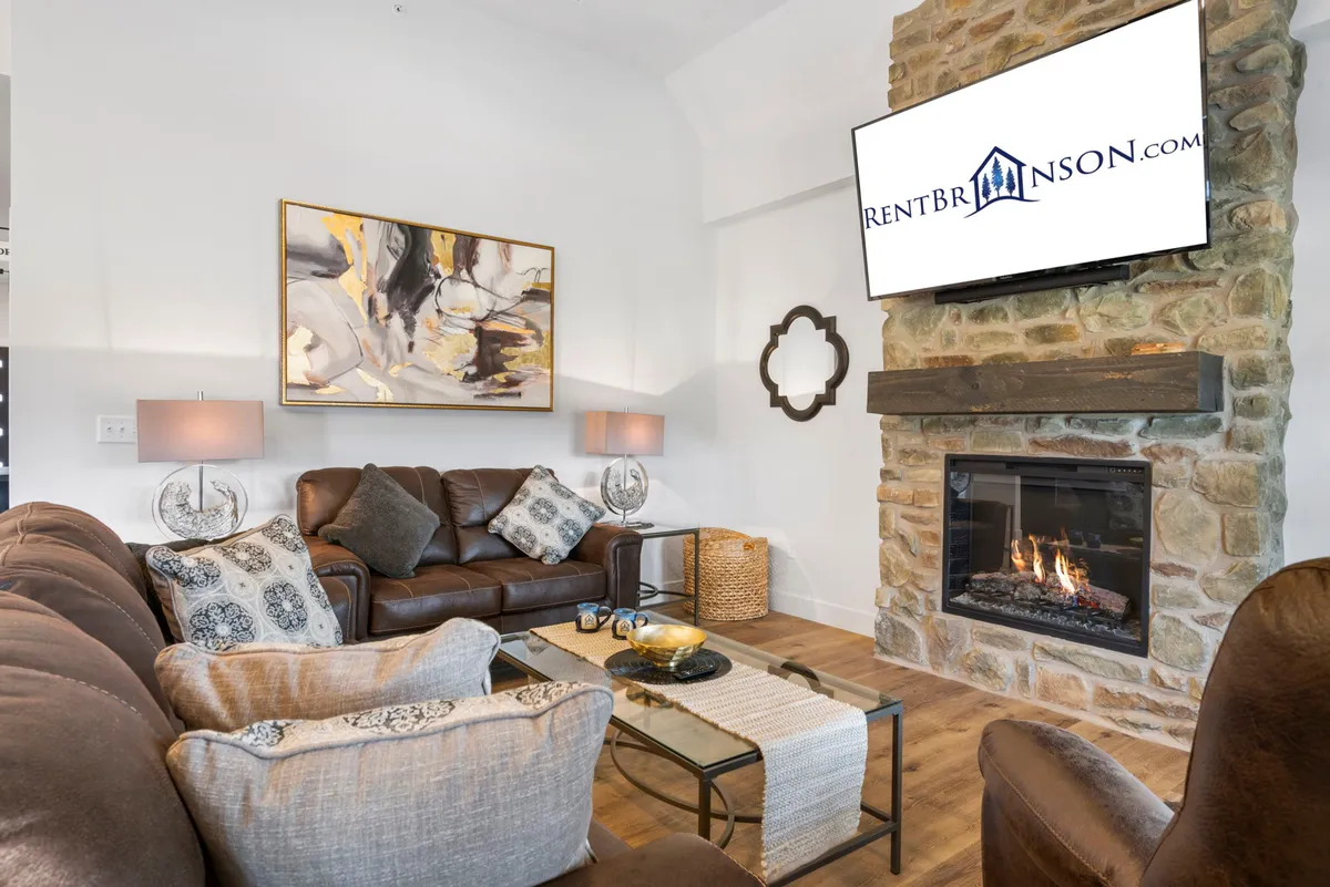 A cozy living room with a leather sofa, warm fireplace, attractive artwork, and a well-styled coffee table. The ambiance invites relaxation, conversation, or enjoying a quiet evening by the fire.