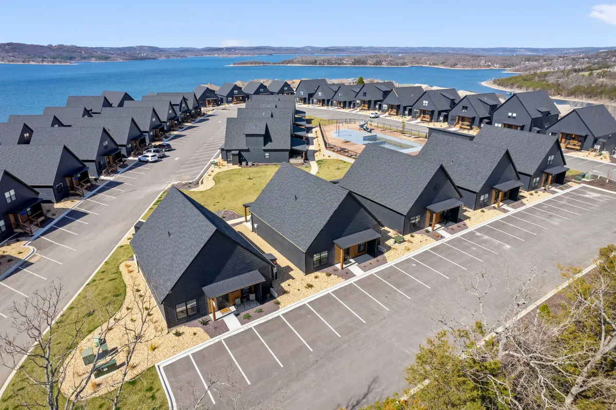 A picturesque view of the lake framed by contemporary architecture and a neatly maintained parking lot. Families gather for picnics and outdoor activities, showcasing the vibrant, social aspect of the neighborhood.