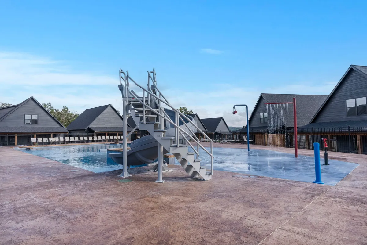 An inviting exterior pool area featuring a water slide, basketball hoop, and ample space for children to play and adults to relax. The scene feels playful and inclusive, highlighting group activities and sunny day enjoyment.