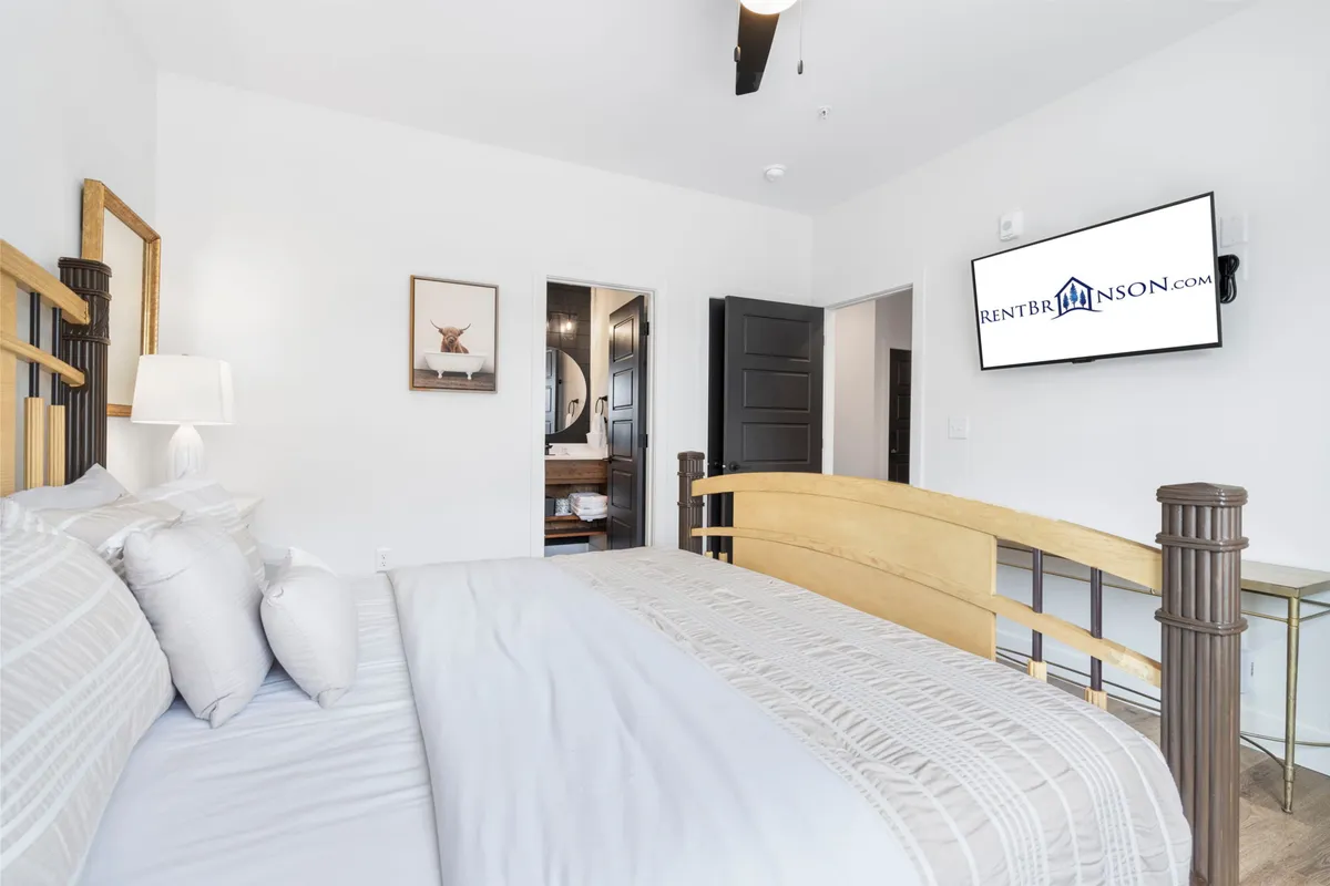 This tranquil bedroom offers a cozy king bed adorned with decorative pillows, a television for evening relaxation, framed artwork, and a doorway that leads directly to a private bathroom. The atmosphere is serene and welcoming.