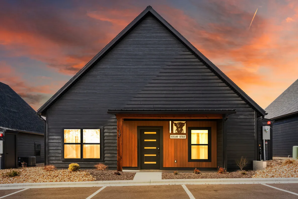 A welcoming exterior view of the home's front door, framed by wooden accents and large windows. The image captures a cozy porch where one can imagine relaxing with a pet, watching the sunset, or preparing for a stroll around the neighborhood.