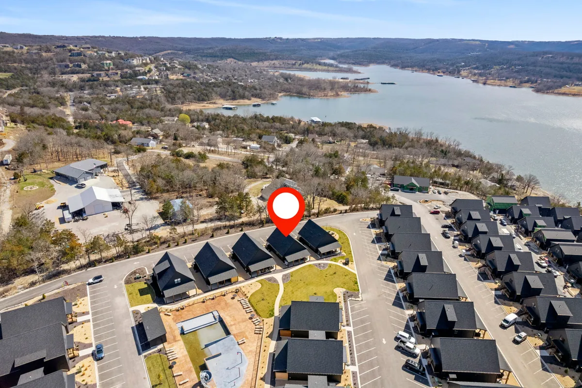 A tranquil lakeshore scene with Table Rock Lake in the background, nearby houses nestled along the water, an inviting outdoor seating area, and a roadway providing easy access to the lake. The scene is set in the golden light of sunset, with green spaces for children to play and space for relaxing by the water.