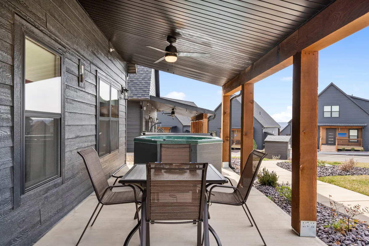 A casual and welcoming outdoor space displaying a hot tub next to an outdoor dining table under a covered patio area. The scene evokes comfort and flexibility for relaxing, dining, or enjoying the fresh air with loved ones or a pet.