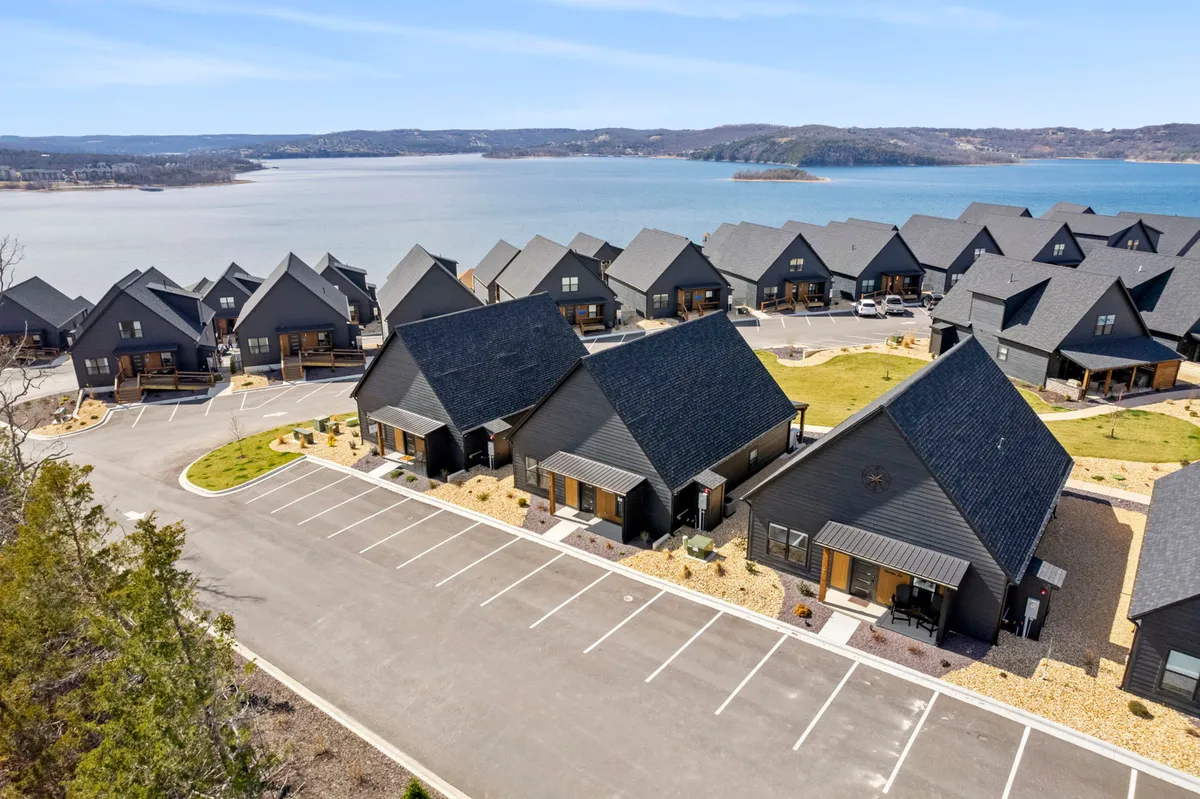Modern cabins are positioned along a landscaped area with a clear view of the lake in the background. The scene conveys the relaxed lifestyle of a vacation community, with opportunities for boating, fishing, and enjoying nature.
